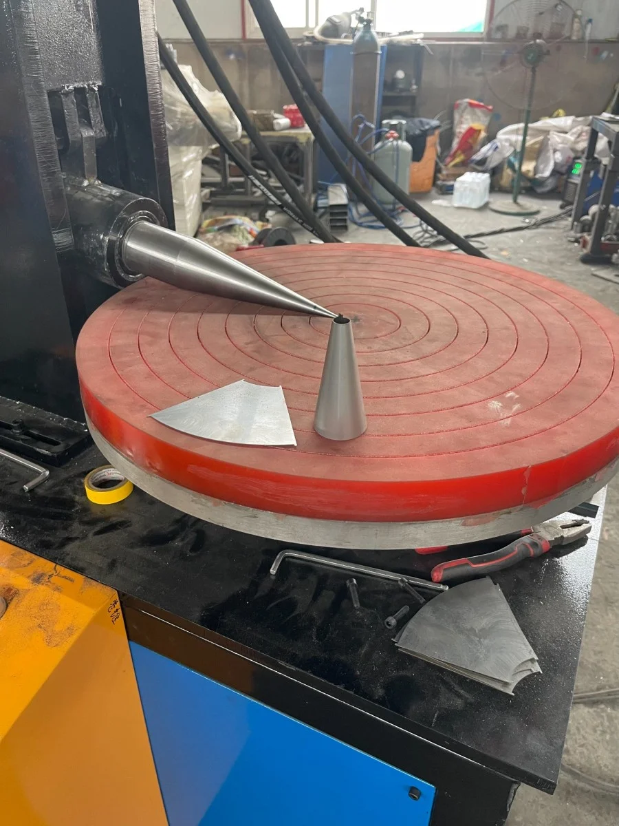 Сине-черный конусопрокатный станок дискового типа, на рабочем столе которого видны небольшие конические формы из нержавеющей стали и технологические инструменты.