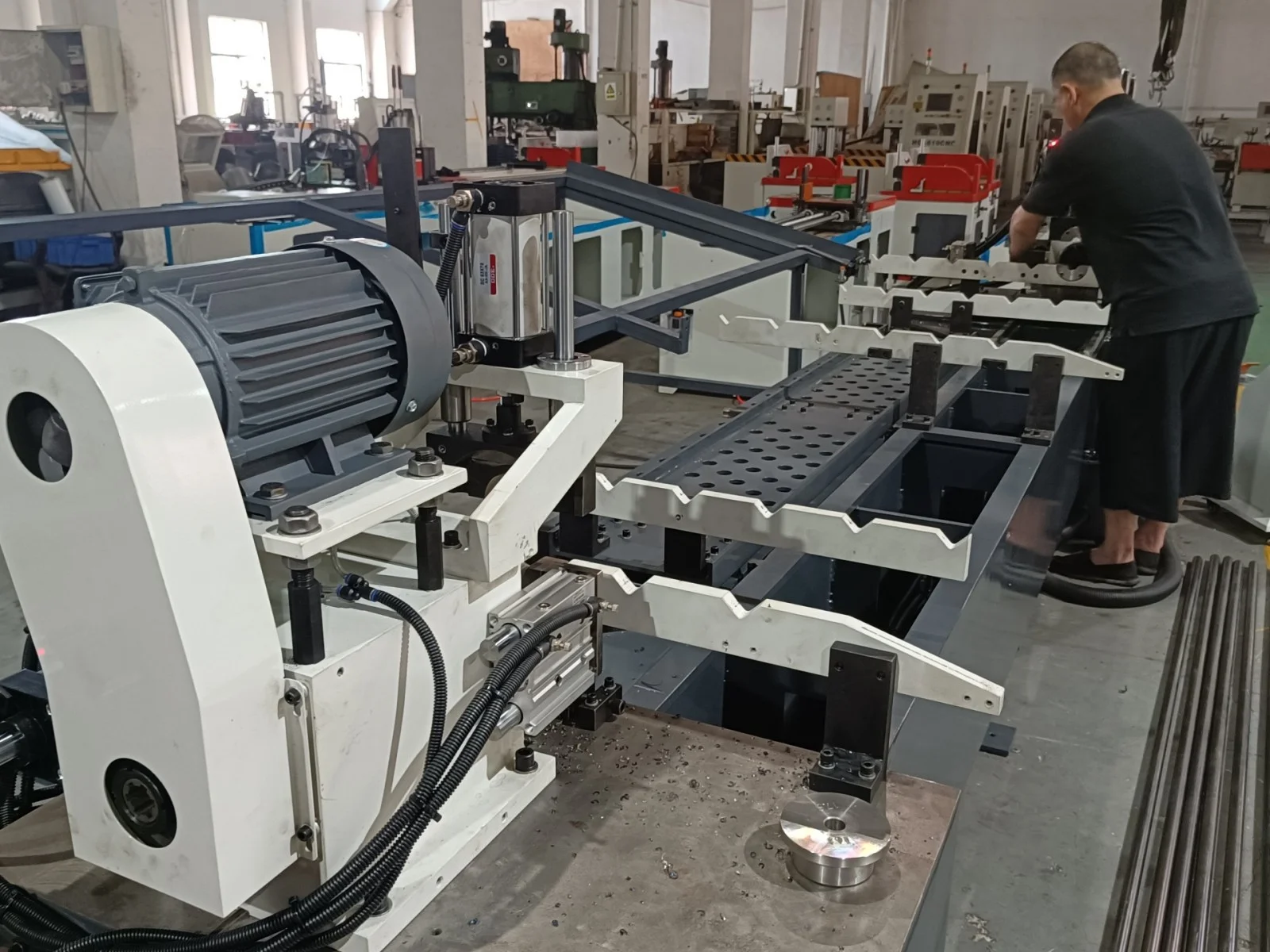 workpiece loading station of double head chamfering machine showing worker operation and round bar stock to be processed